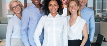 Smiling young mixed race female leader standing looking at camera with diverse team people, happy african american employee business coach millennial professional with office workers group portrait